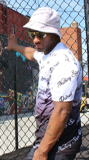 Man standing against fence wearing a Nothing Stops Detroit Terry Cloth Bucket Cap